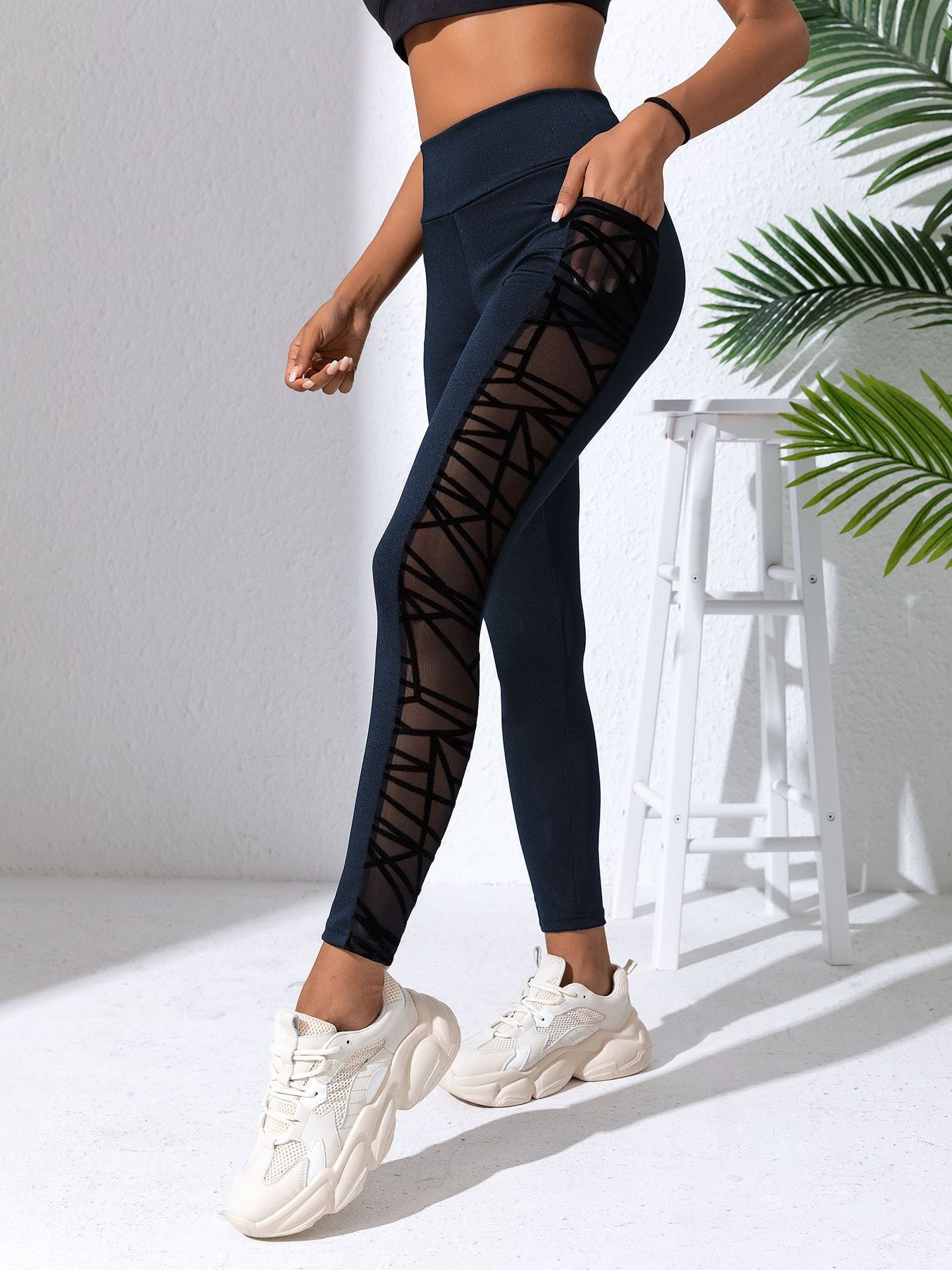 Person wearing navy leggings with sheer mesh panels in a minimal indoor setting.
