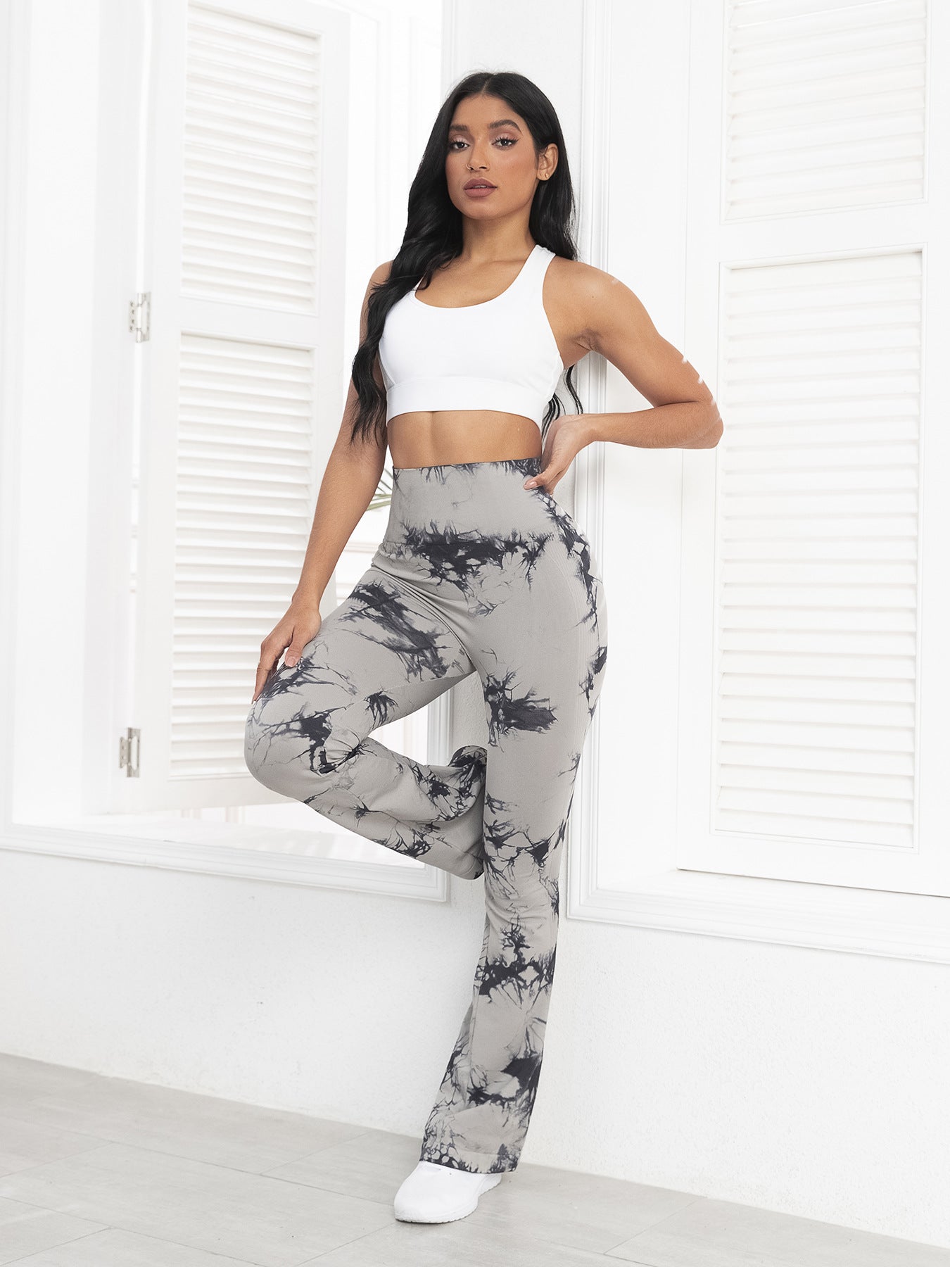Woman wearing a white crop top and gray tie-dye pants in a minimalistic room.
