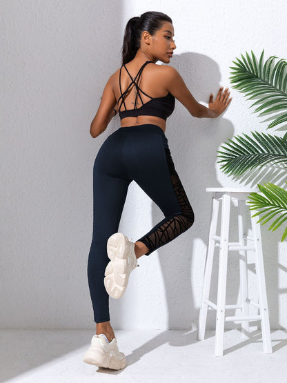 Woman in black athletic wear posing against a white wall with greenery.