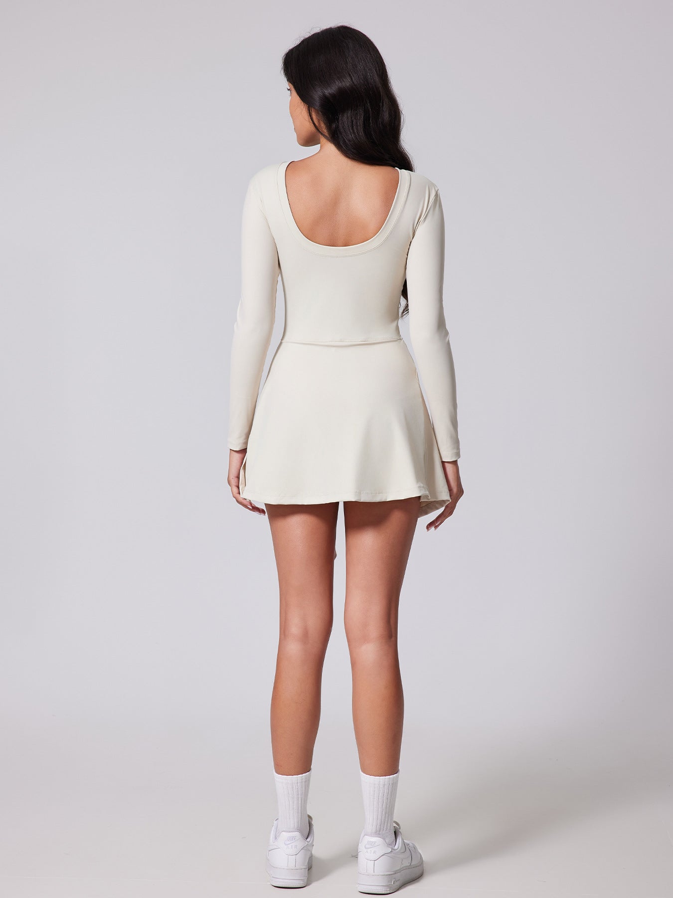 Woman wearing a white long-sleeve dress on a plain background