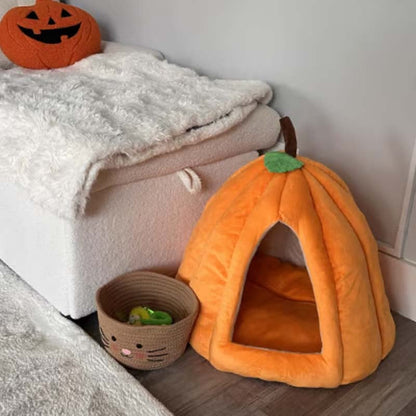Orange pumpkin-shaped pet bed next to a white blanket and small basket on a wooden floor.