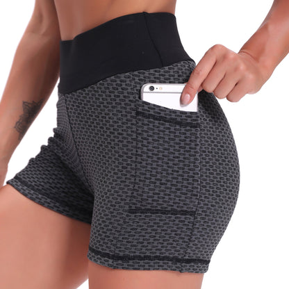 Person wearing black patterned shorts with a pocket holding a phone on a white background