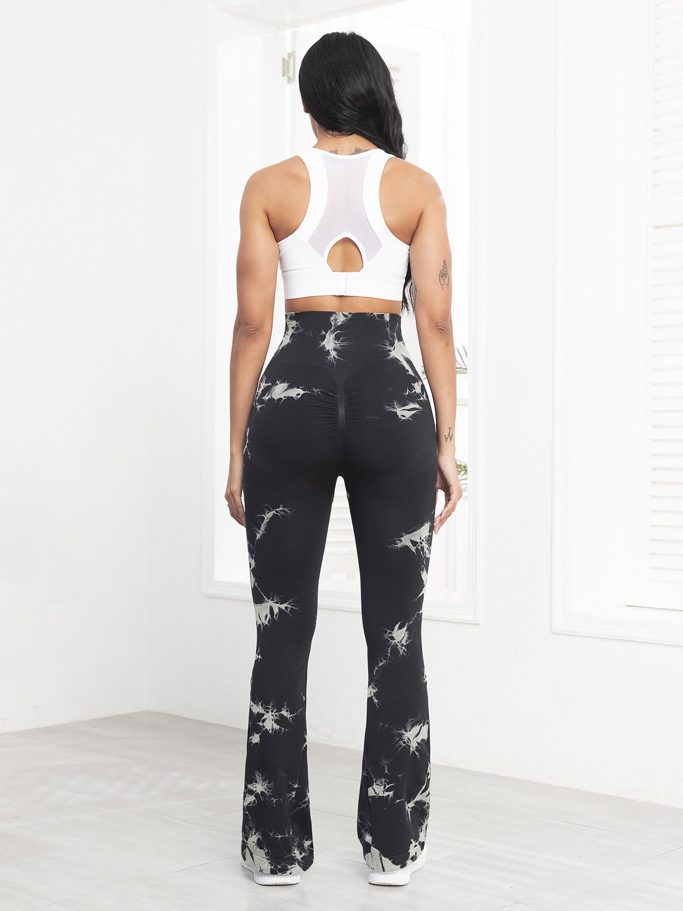 Person wearing black tie-dye leggings and a white crop top in a minimalistic setting