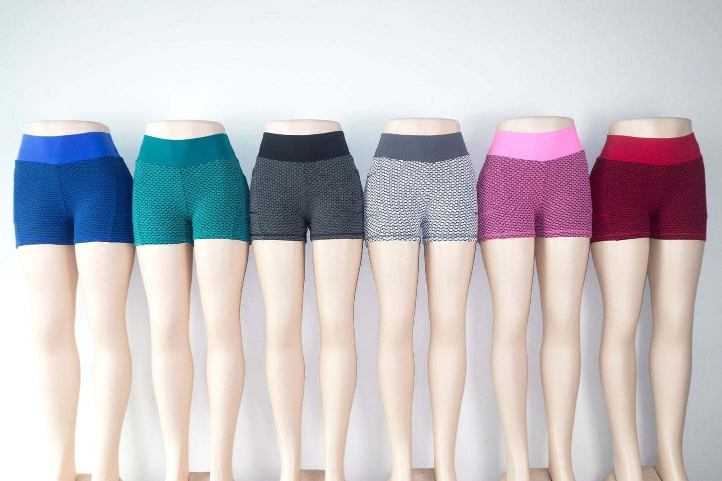 Row of mannequins wearing colorful shorts against a plain background