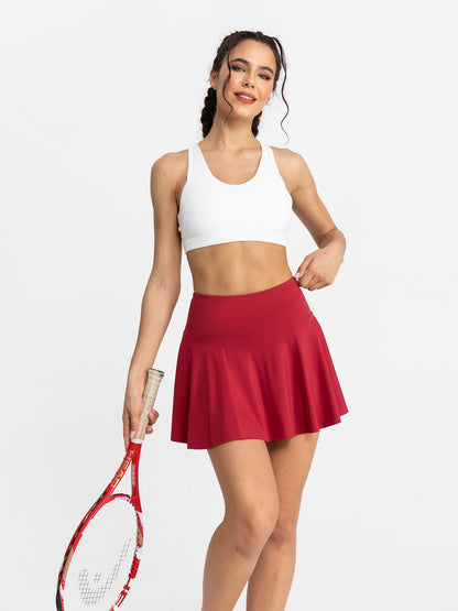 Woman in white sports bra and red tennis skirt holding a racket on a white background