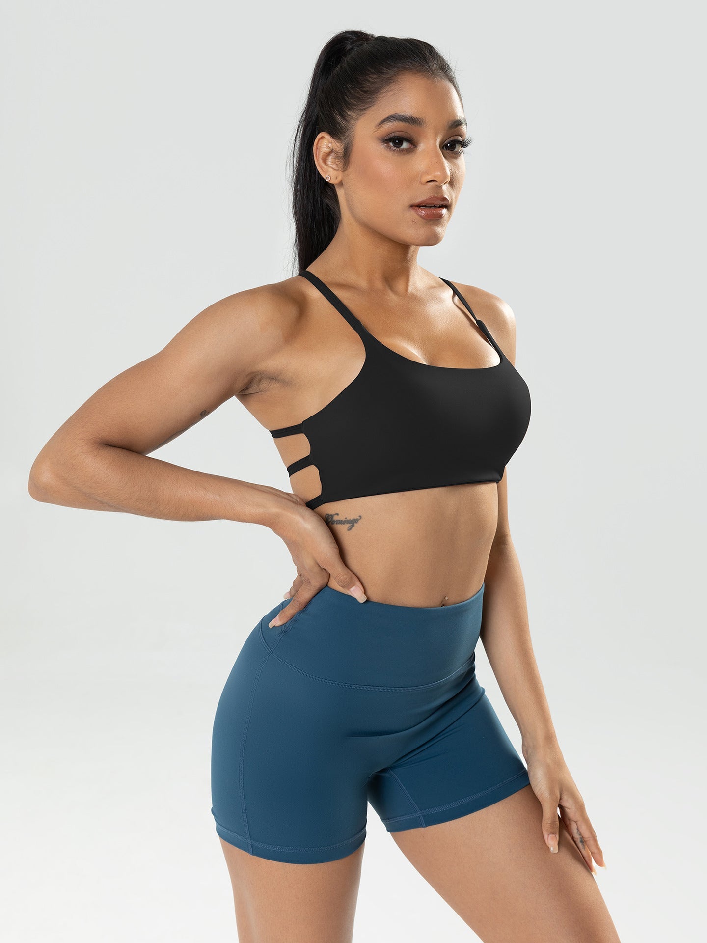 Woman wearing a black sports bra and blue shorts on a gray background