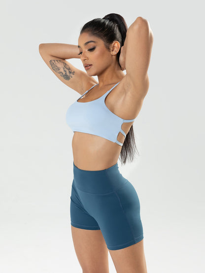 Woman wearing a light blue sports bra and dark blue shorts on a white background