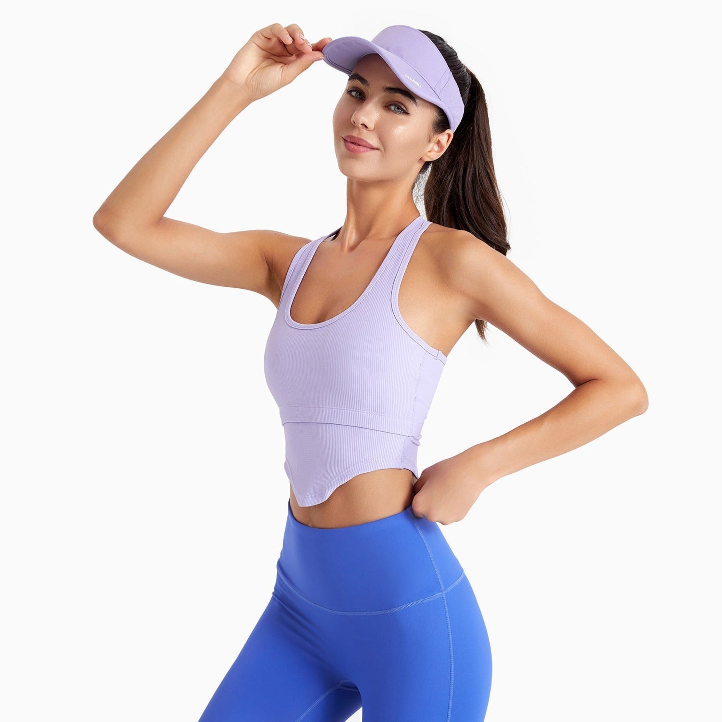 Woman wearing a purple sports bra and blue leggings with a matching visor on a white background