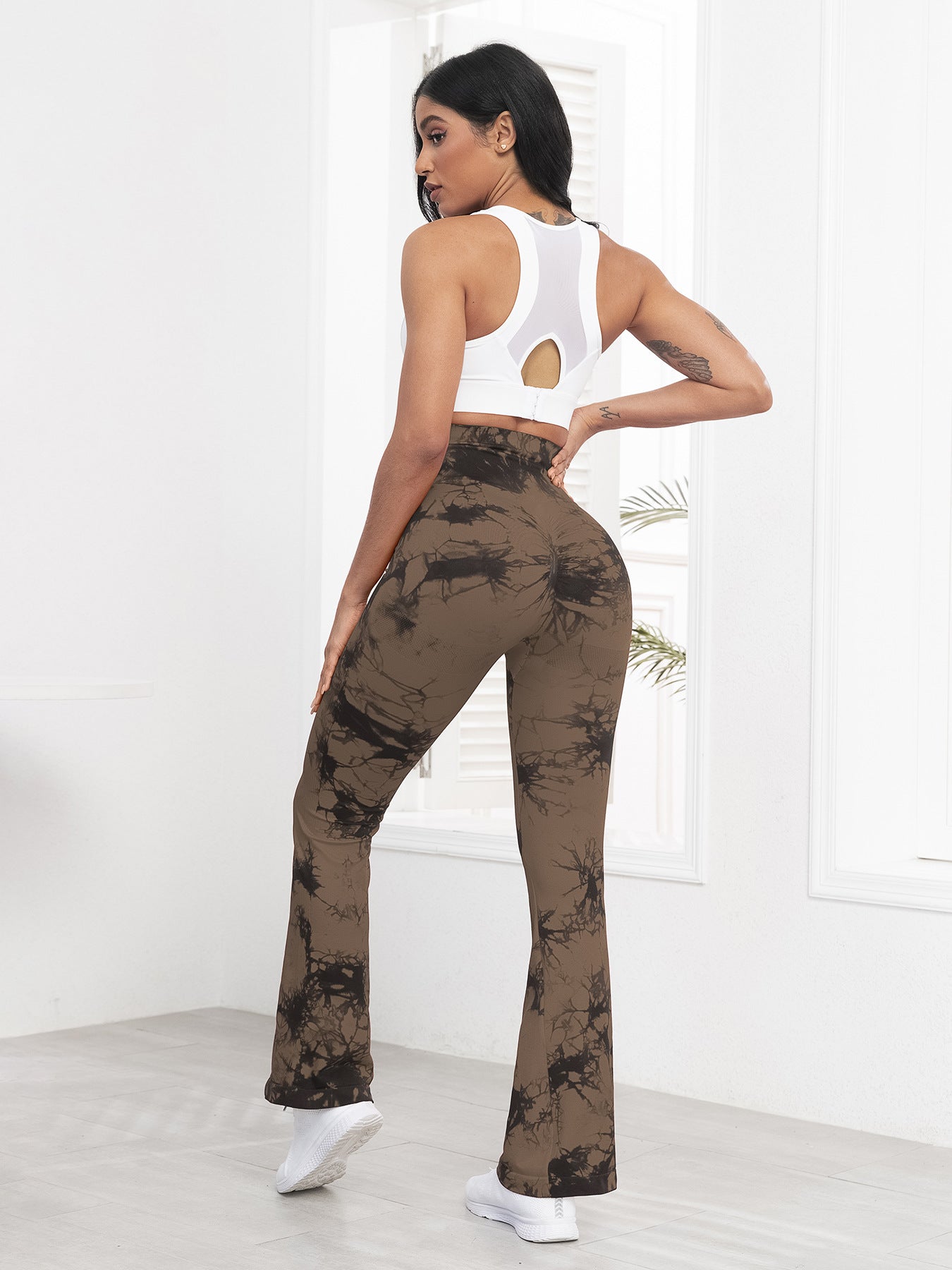 Woman wearing a white crop top and brown tie-dye pants against a white background