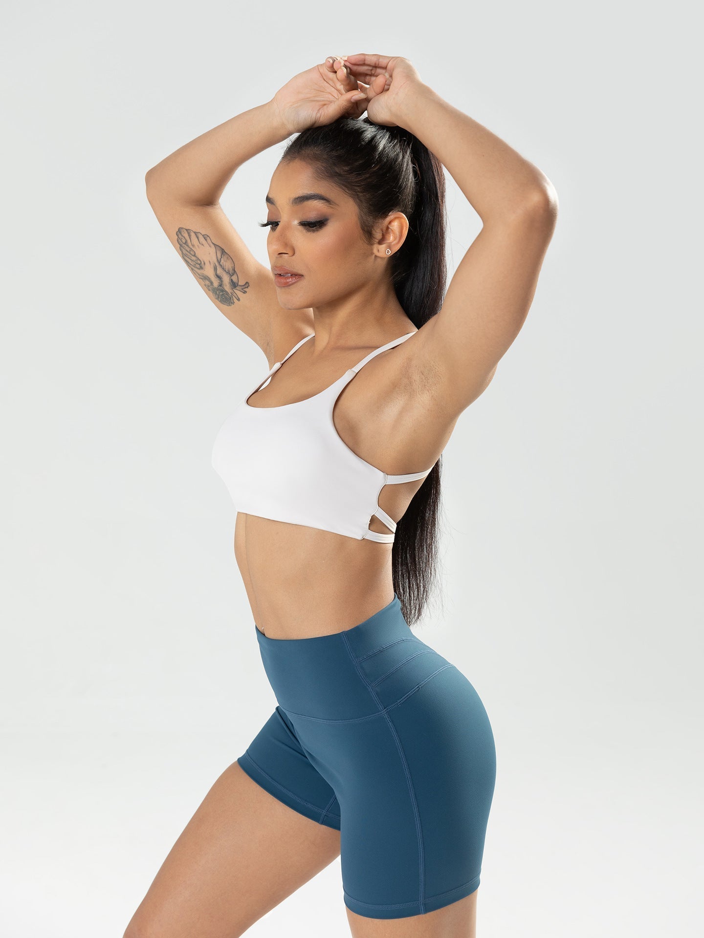 Woman wearing a white sports bra and blue shorts on a light gray background