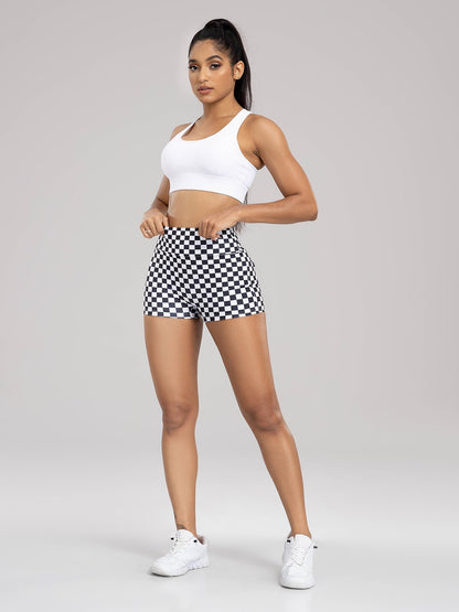Woman wearing a white sports bra and checkered shorts on a gray background