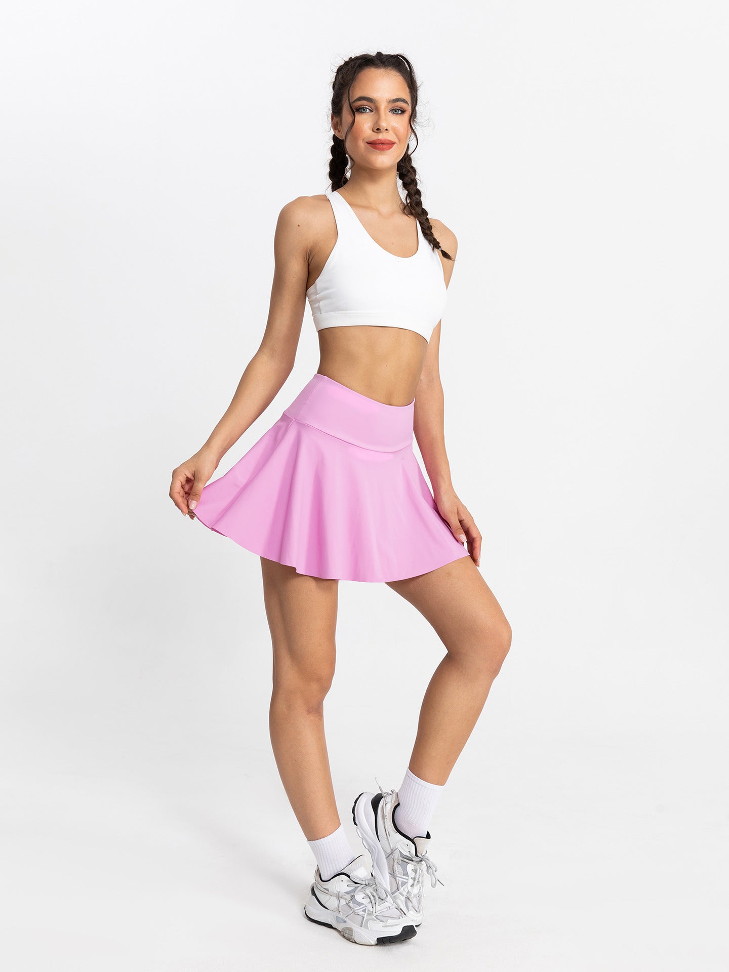 Woman wearing a white sports bra and pink tennis skirt on a white background