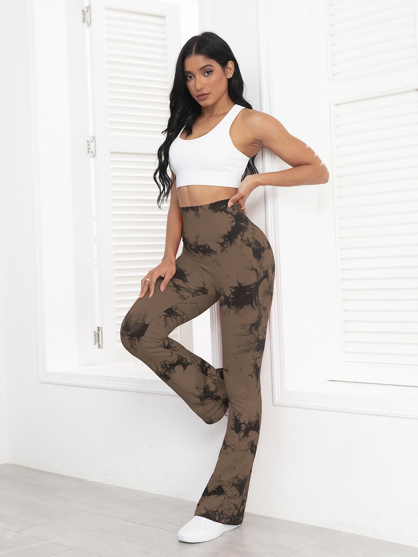 Woman wearing a white top and brown tie-dye pants in a minimalistic setting