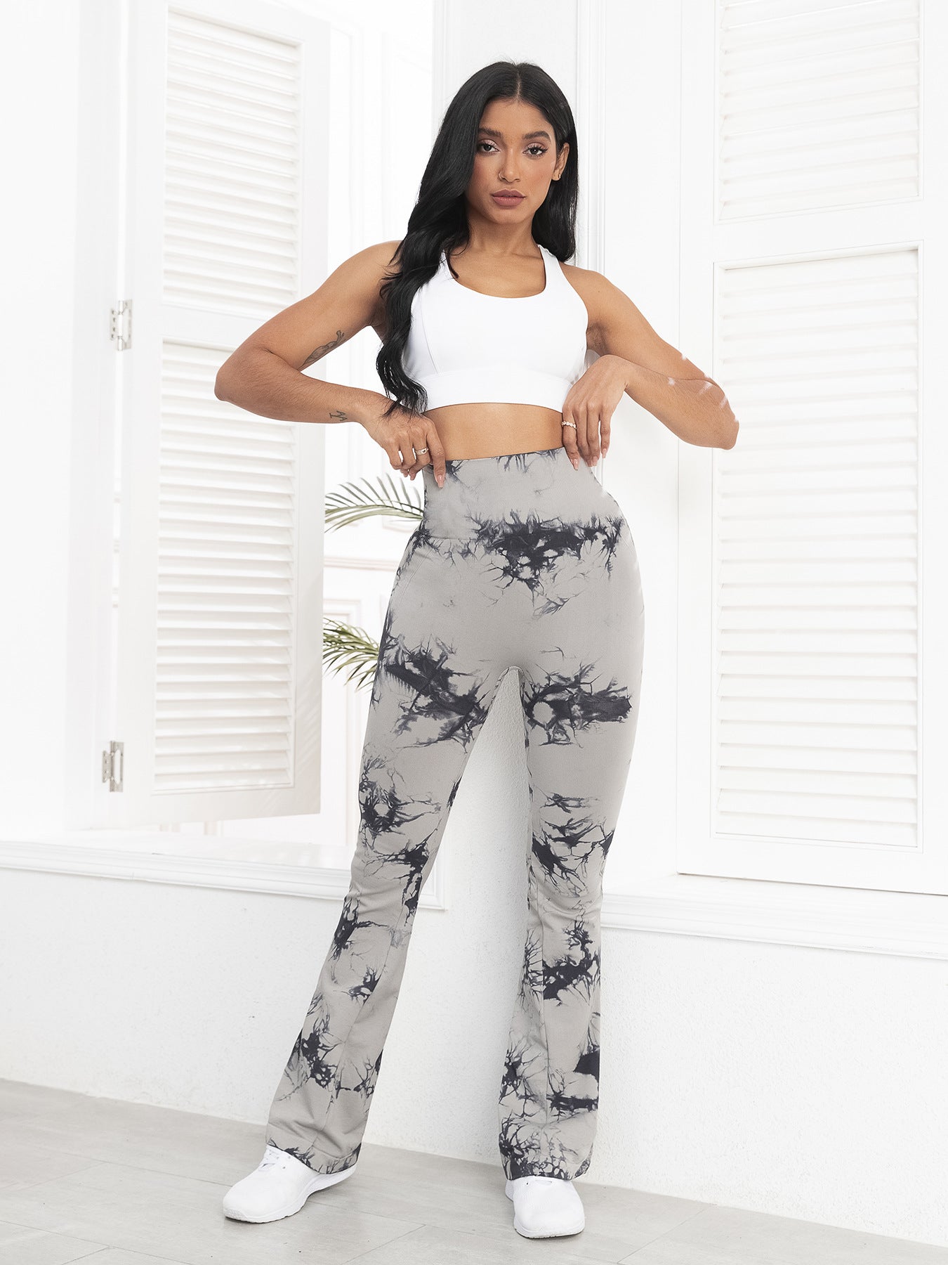 Woman wearing a white top and gray tie-dye pants in a minimalistic room.
