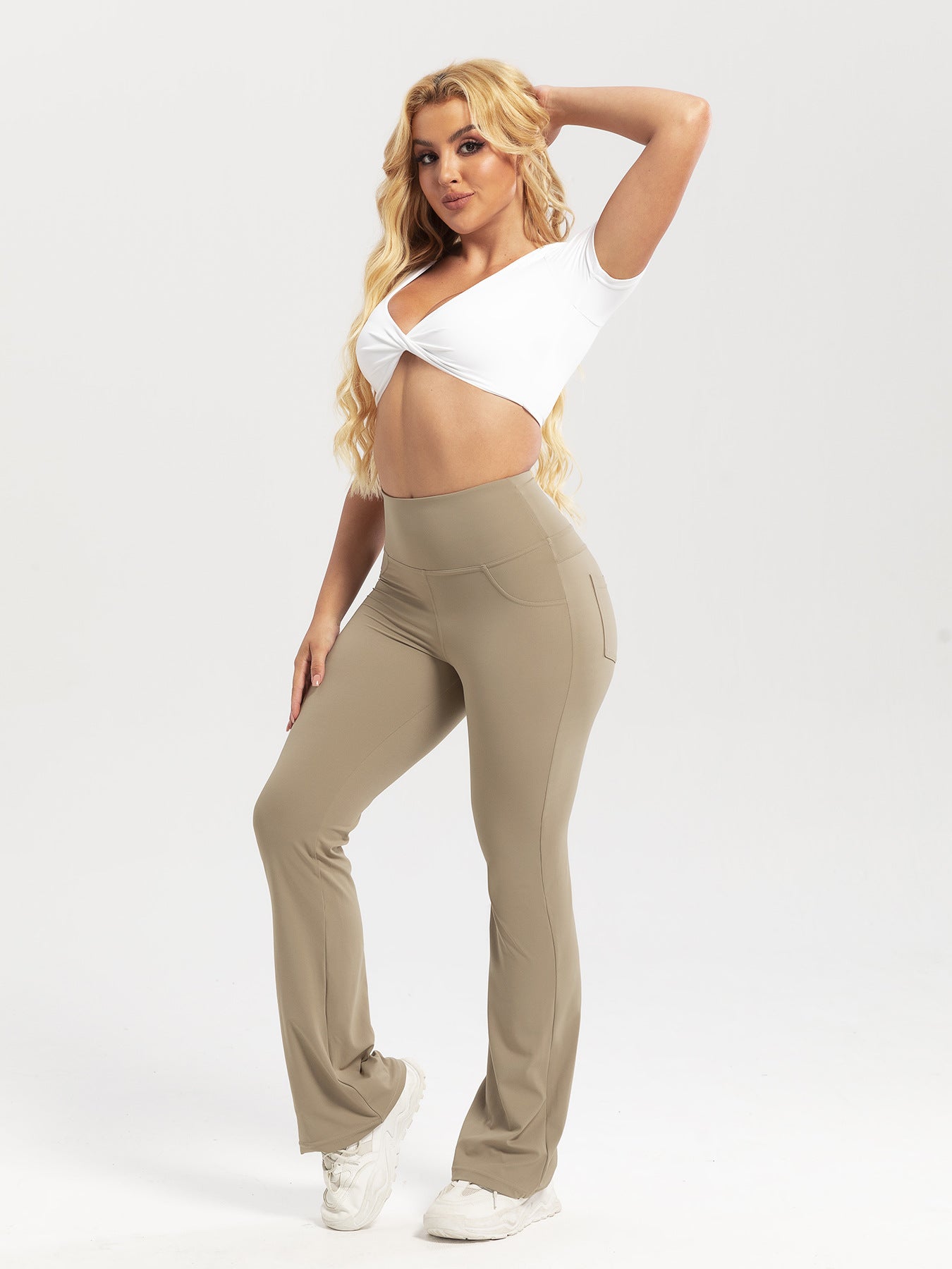 Woman wearing beige pants and a white top on a plain background