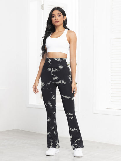 Woman wearing black tie-dye leggings and a white top in a minimalistic room.