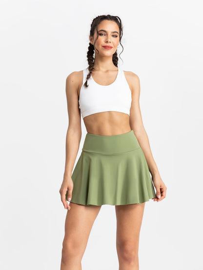 Woman wearing a white sports bra and green skirt on a white background