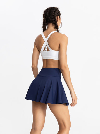 Woman wearing a white sports bra and navy blue skirt on a white background