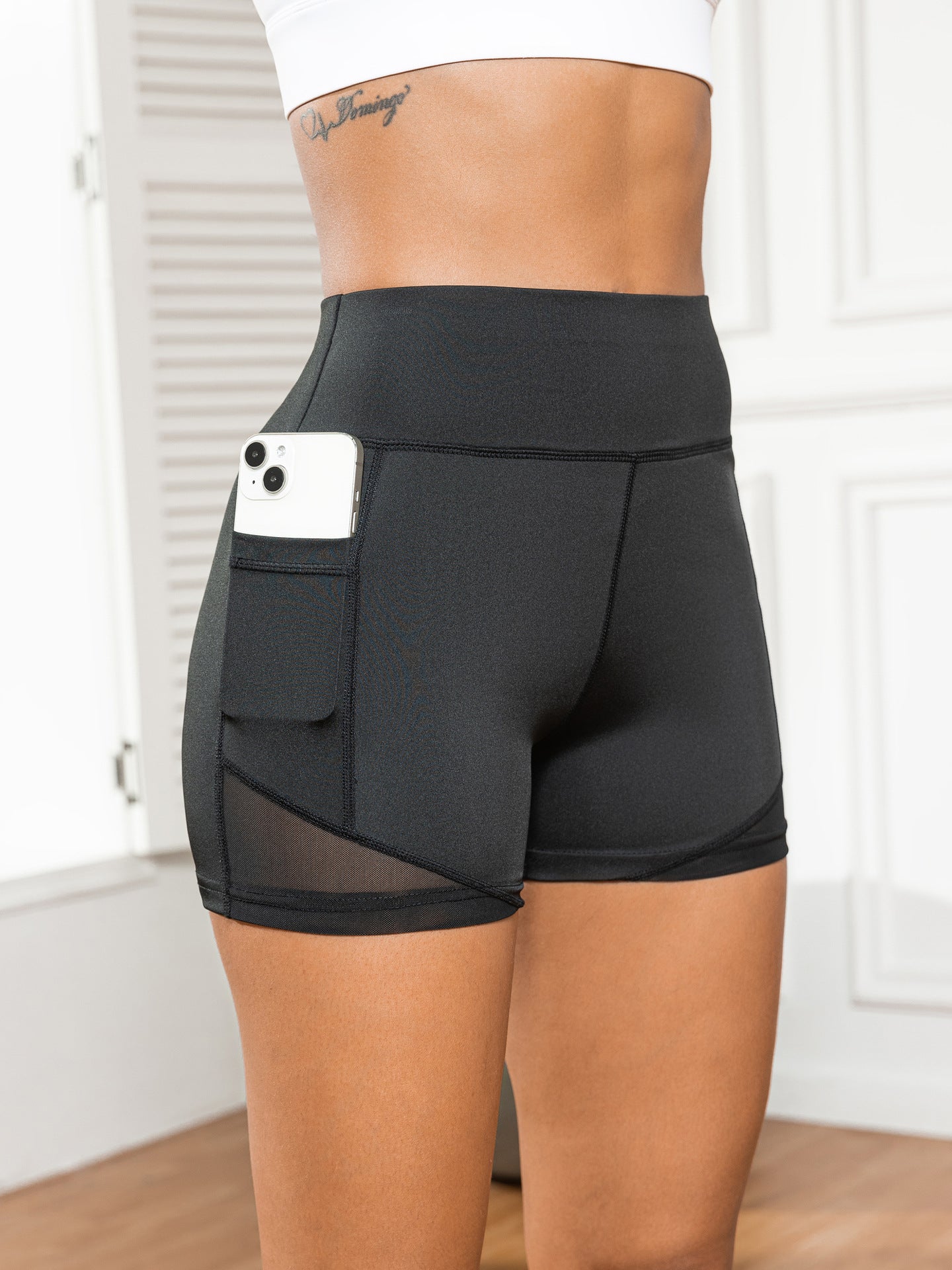 Black athletic shorts with a pocket holding a phone, worn by a person indoors.