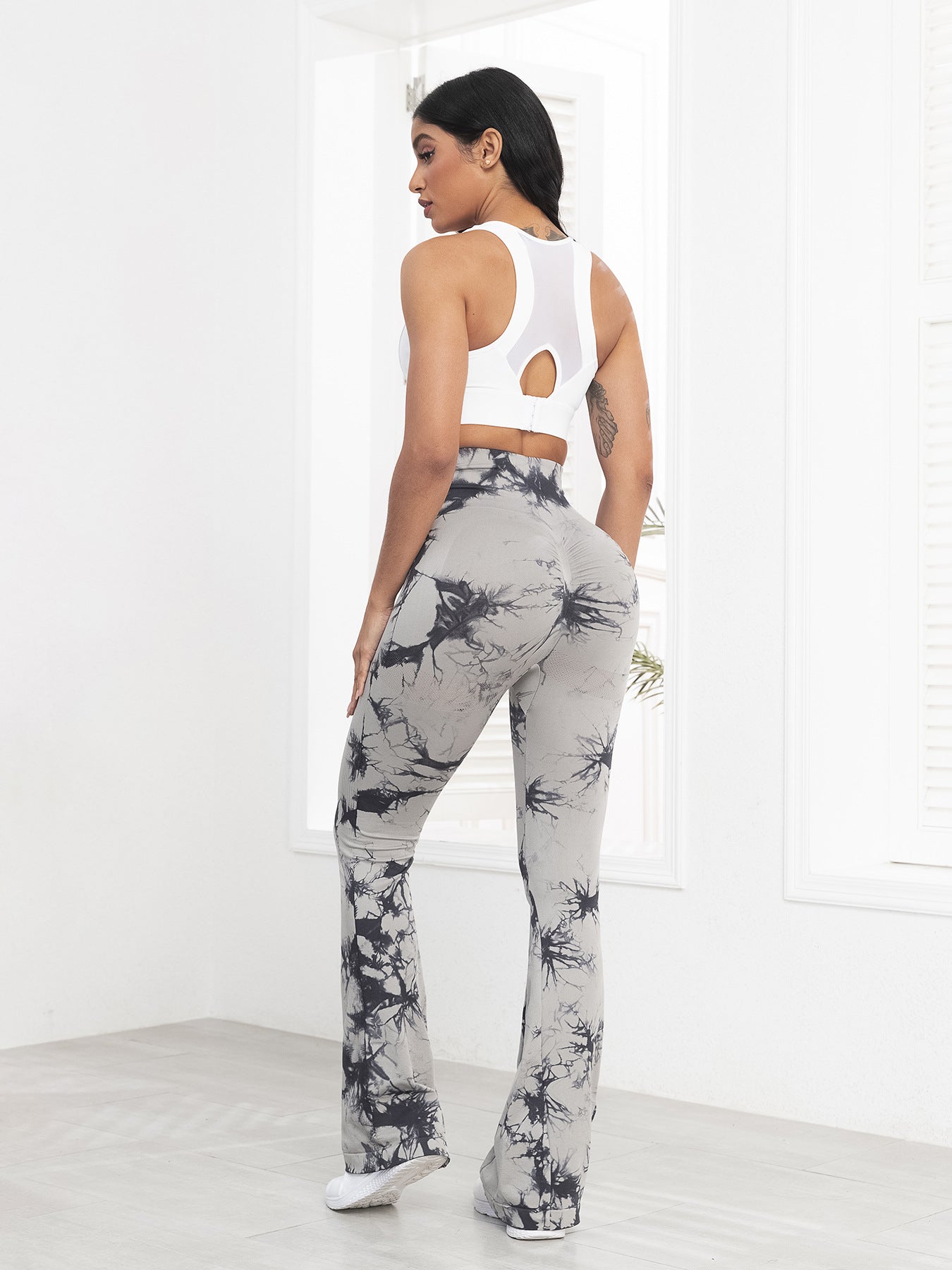 Woman wearing a white sleeveless top and gray tie-dye pants in a minimalistic setting.