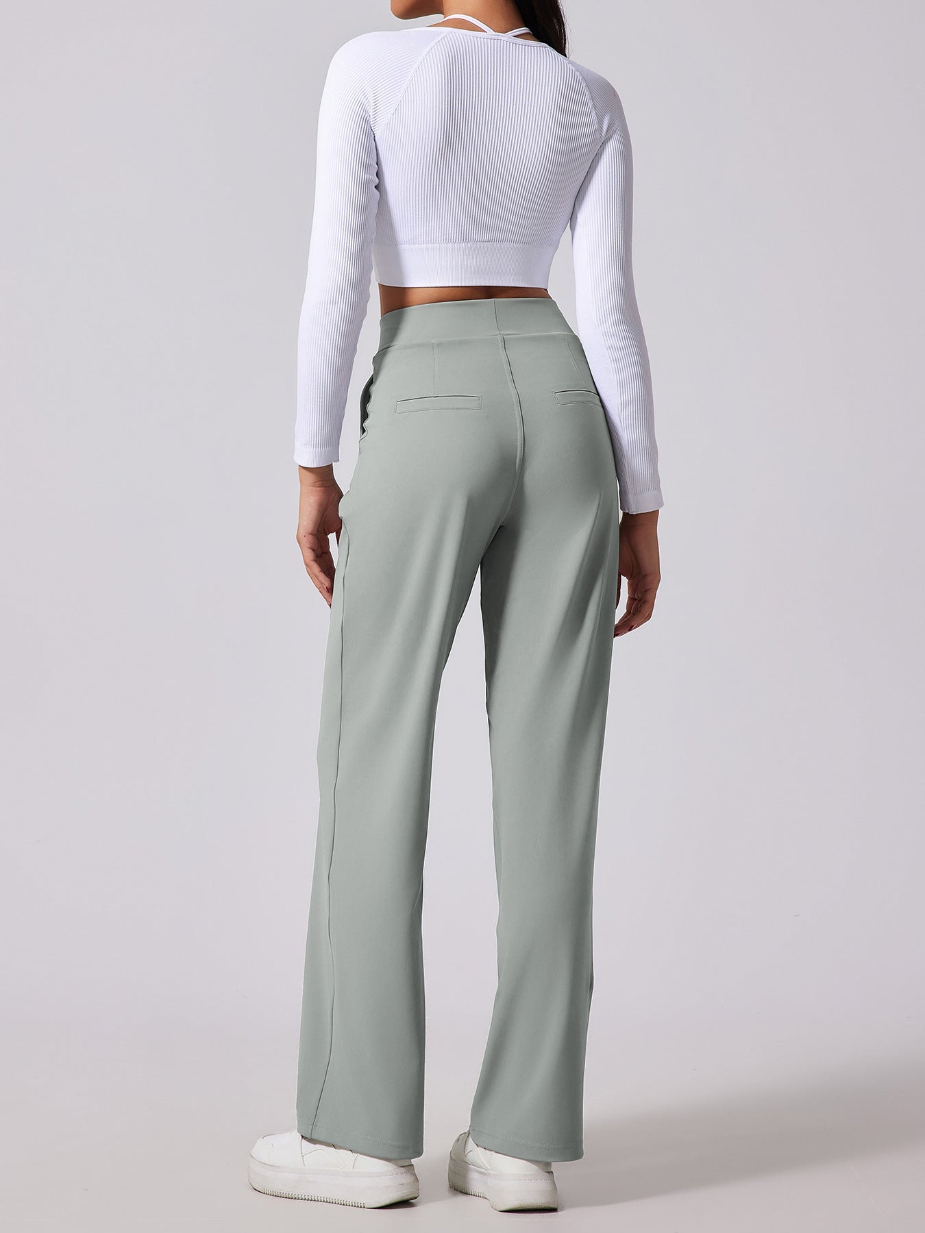 Person wearing a white long-sleeve top and light green high-waisted pants on a plain background