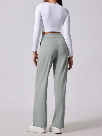 Person wearing a white long-sleeve top and light green high-waisted pants on a plain background