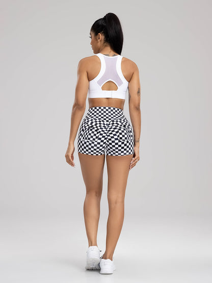 Woman wearing a white sports bra and black and white checkered shorts on a gray background